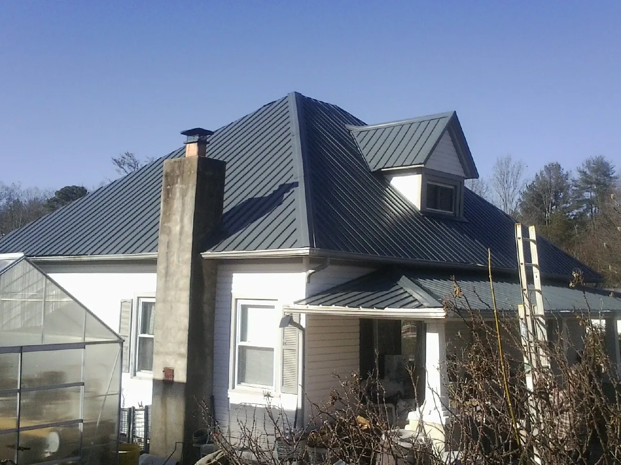 Dark blue standing seam metal roof on a white farmhouse with dormer — Slate & Tile Roof Repair by Roofing Brothers in Morris Chapel