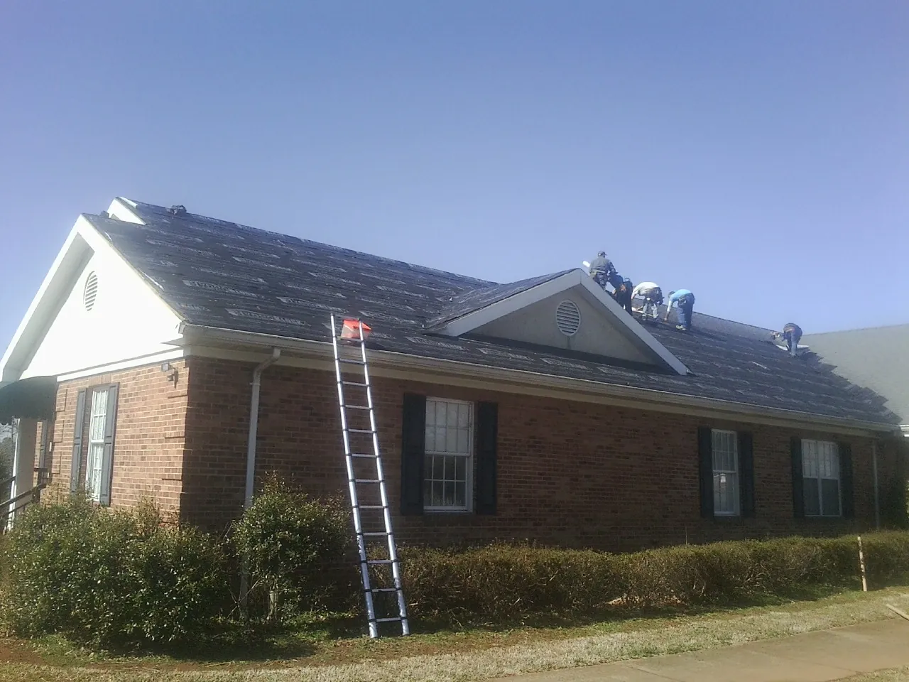 Crew tearing shingles off a brick ranch roof with a ladder set — Emergency Roof Repair work by our crew in Morris Chapel