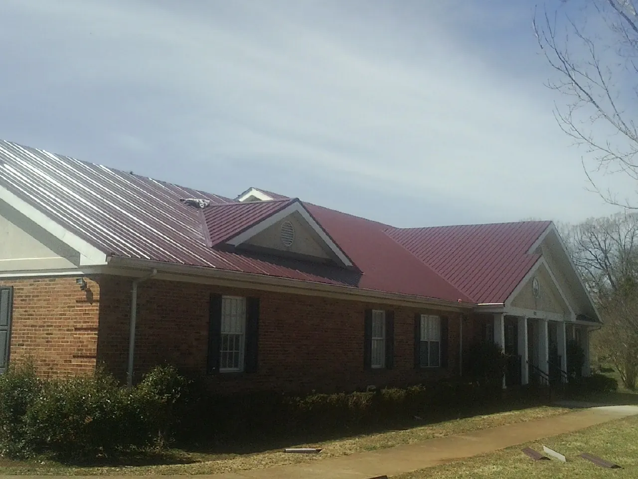 Red metal roof with gabled entries on a long brick building, from a Hail Damage Roof Repair job in Morris Chapel