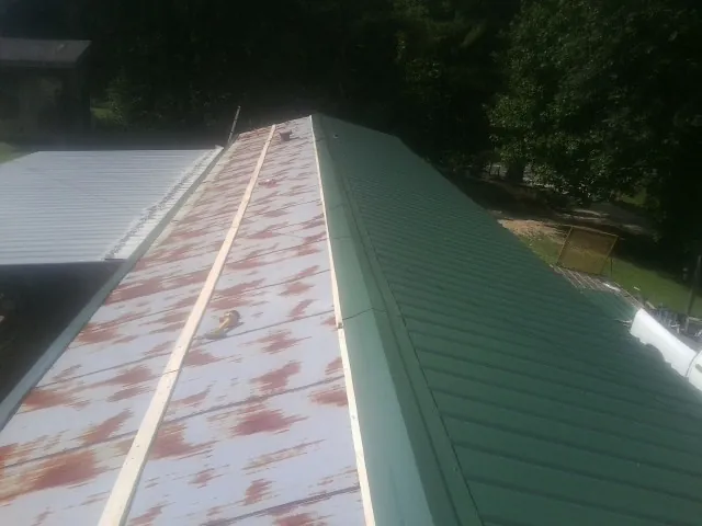 Old rusted panels beside newly installed green metal roofing — Wind Damage Roof Repair by Roofing Brothers in Morris Chapel