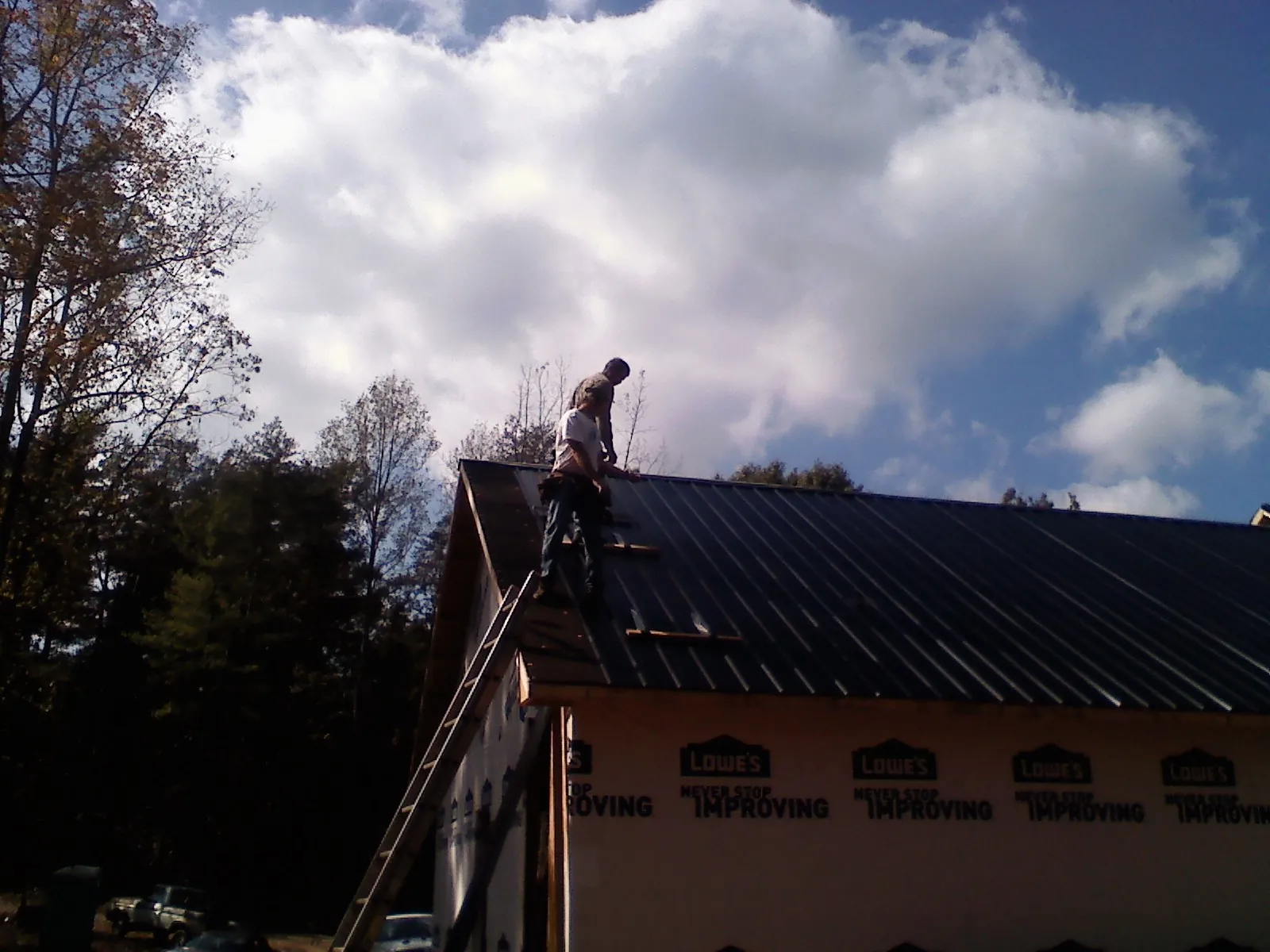 Roofer fastening dark metal panels high against a cloudy sky, from a Roof Inspection job in Morris Chapel