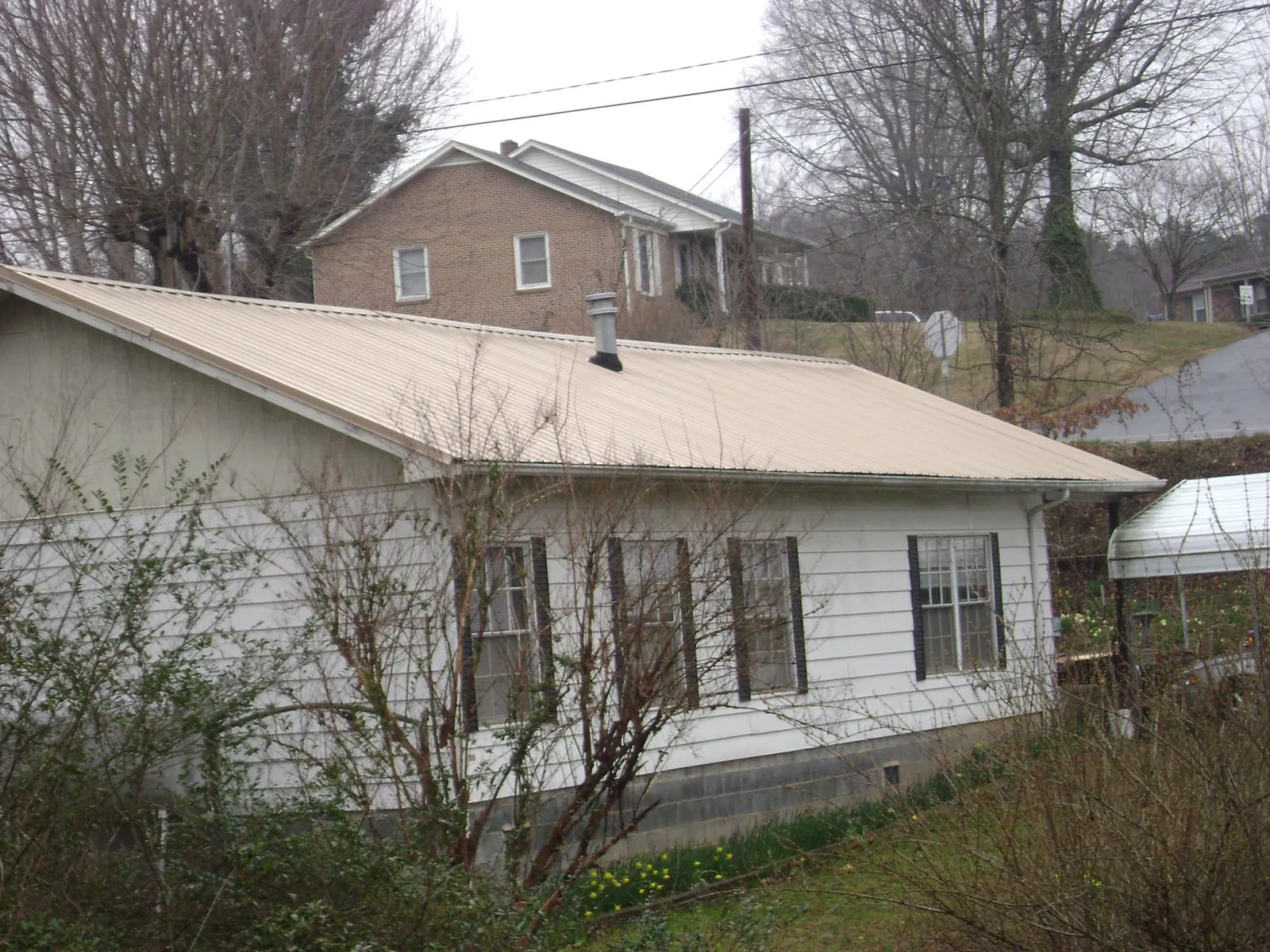 Tan metal roof on a white sided house set into a hillside — Commercial Roofing by Roofing Brothers in Morris Chapel