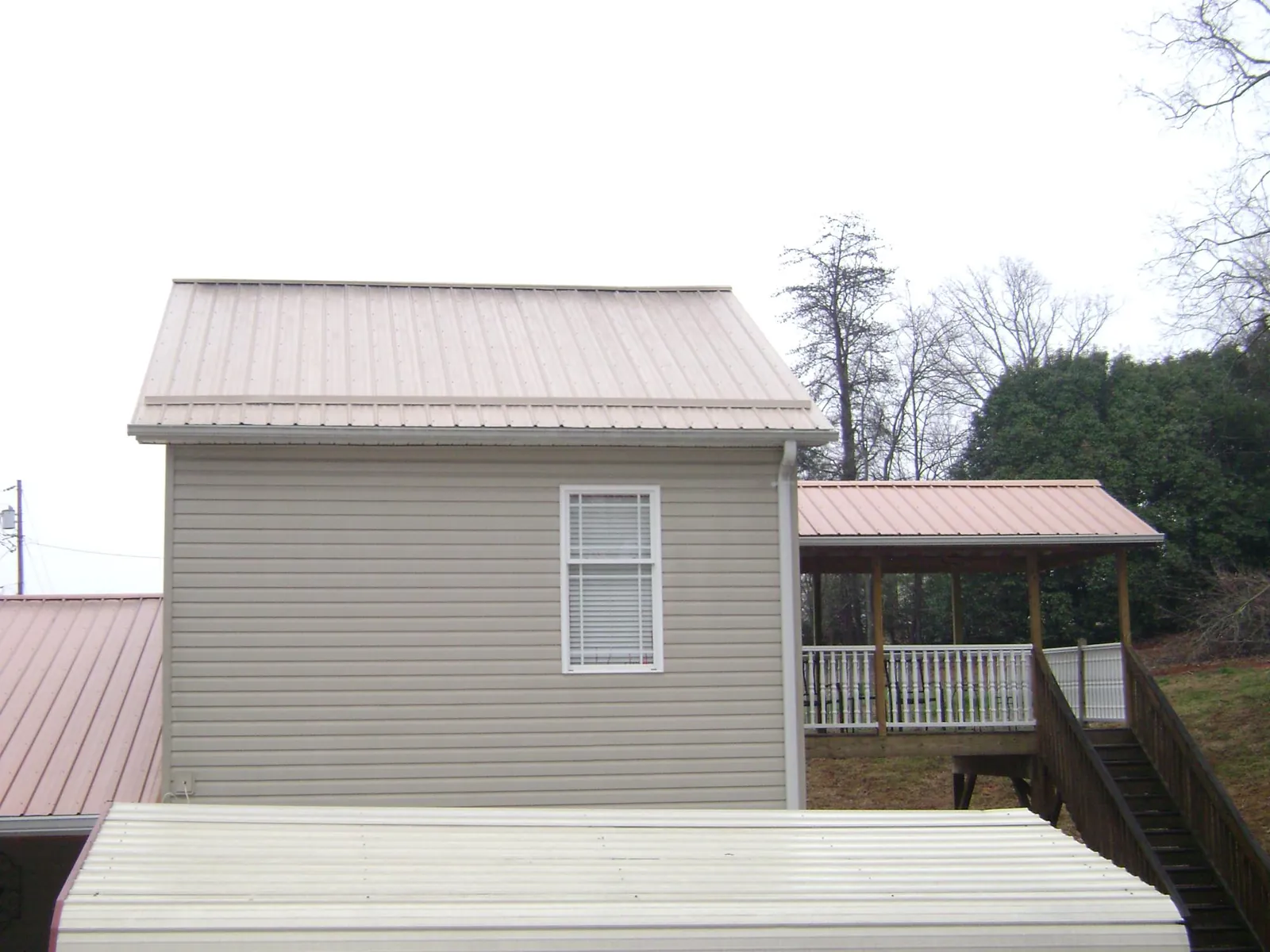 Tan metal roofs on a two story addition and attached porch, from a Roof Replacement job in Morris Chapel